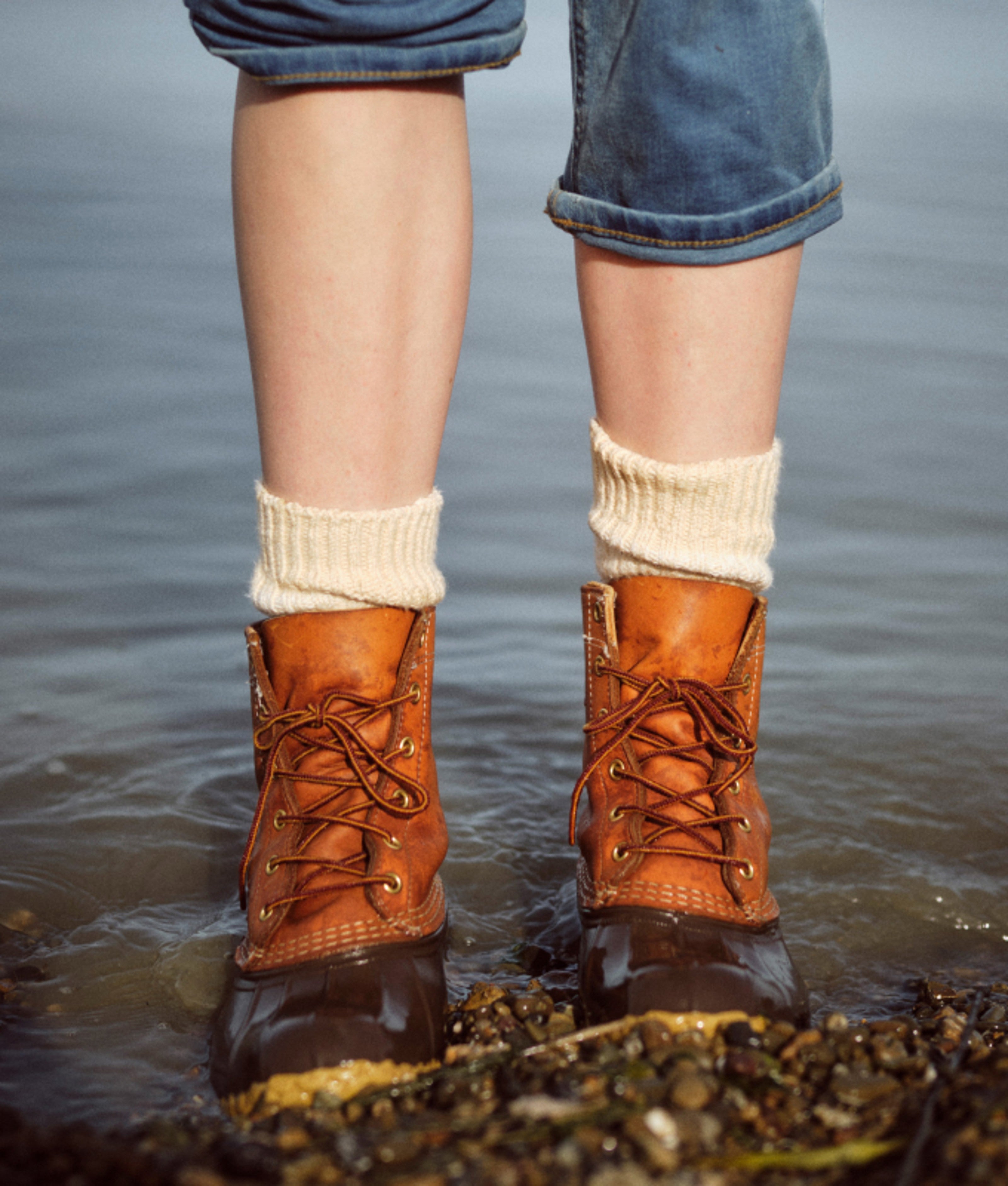 Bean boots worn in shallow water along a rocky shoreline.