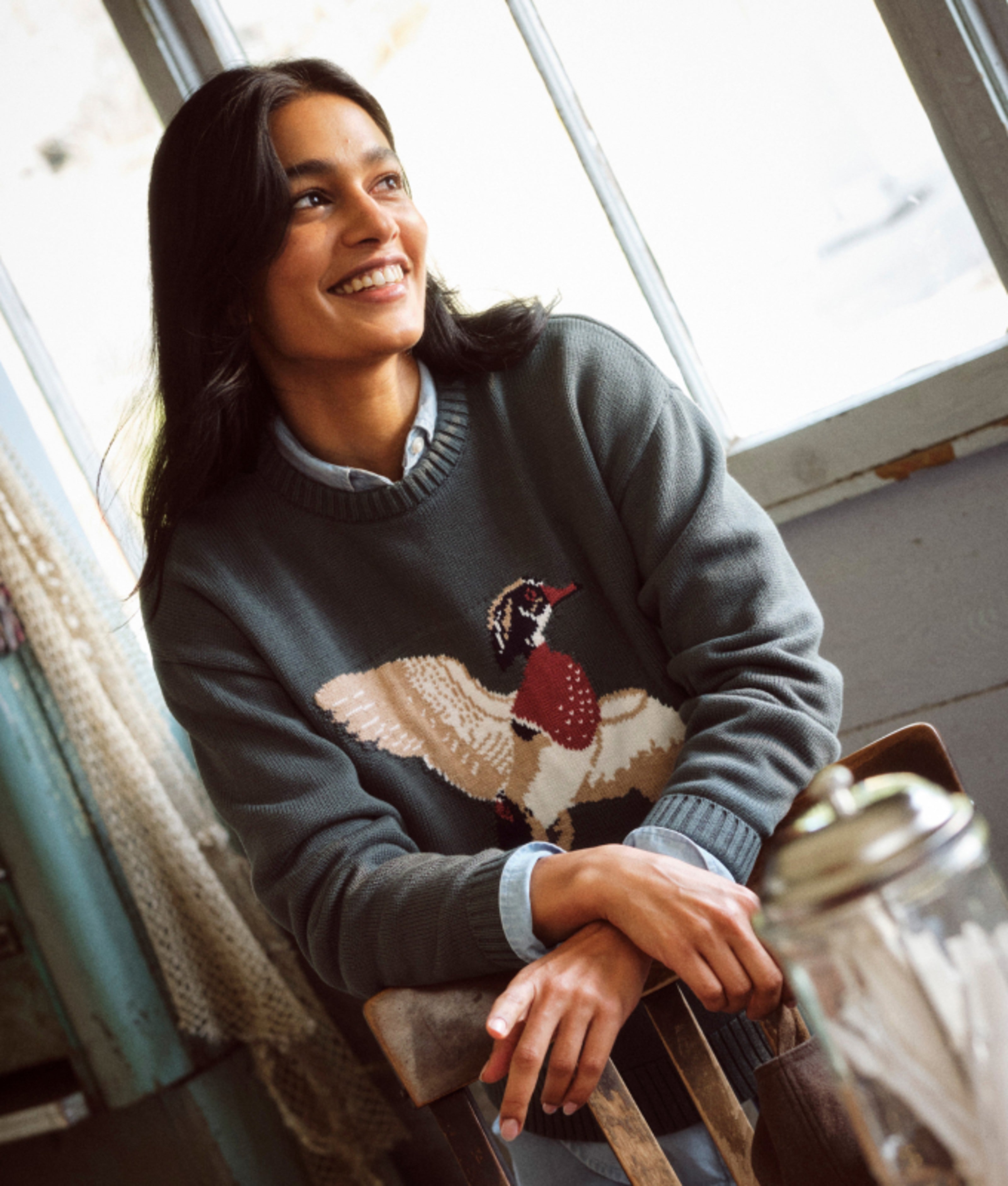 Person seated aboard a boat wearing a sweater with a bird motif.