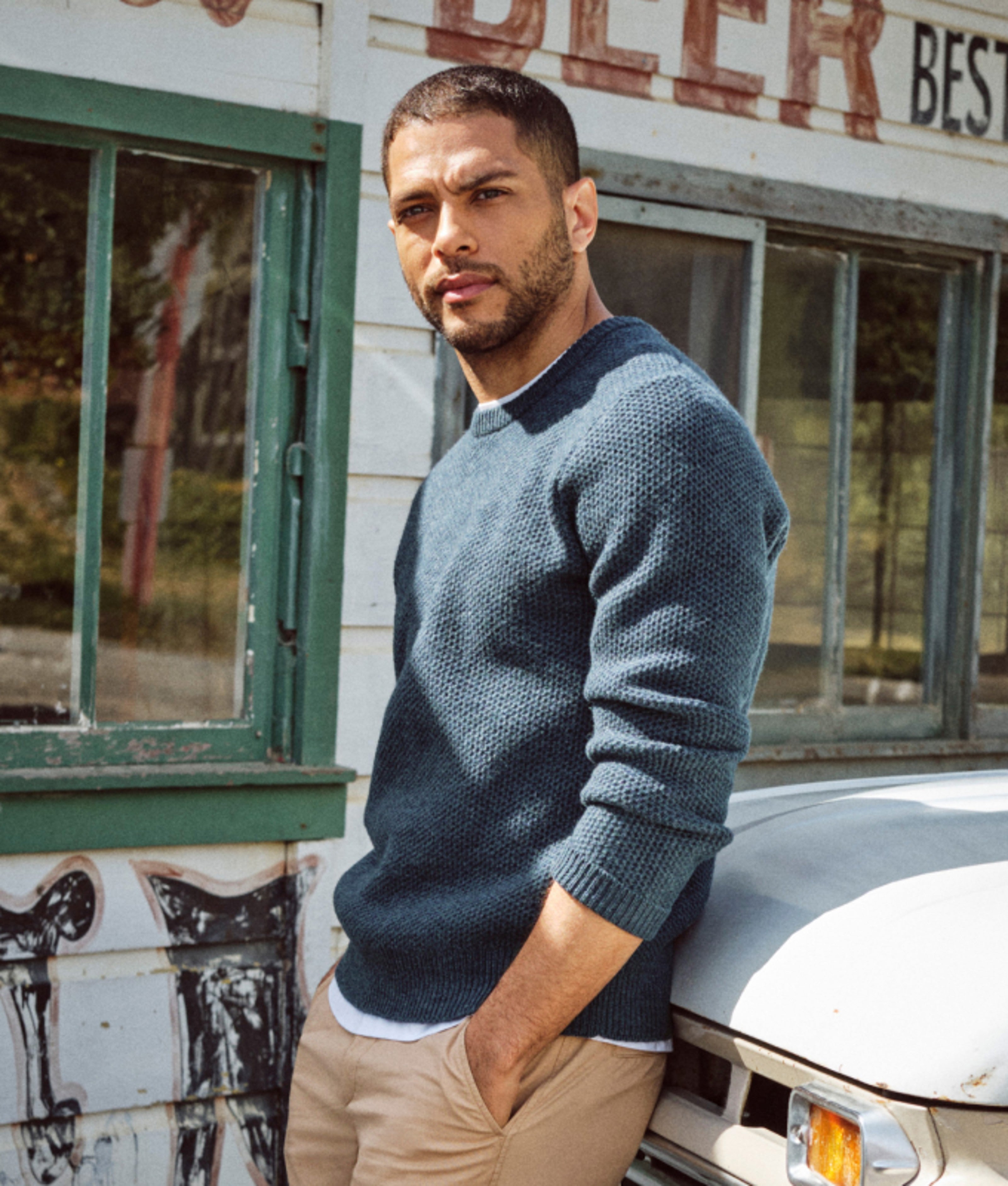 Person in a blue crewneck sweater standing beside a vintage storefront.