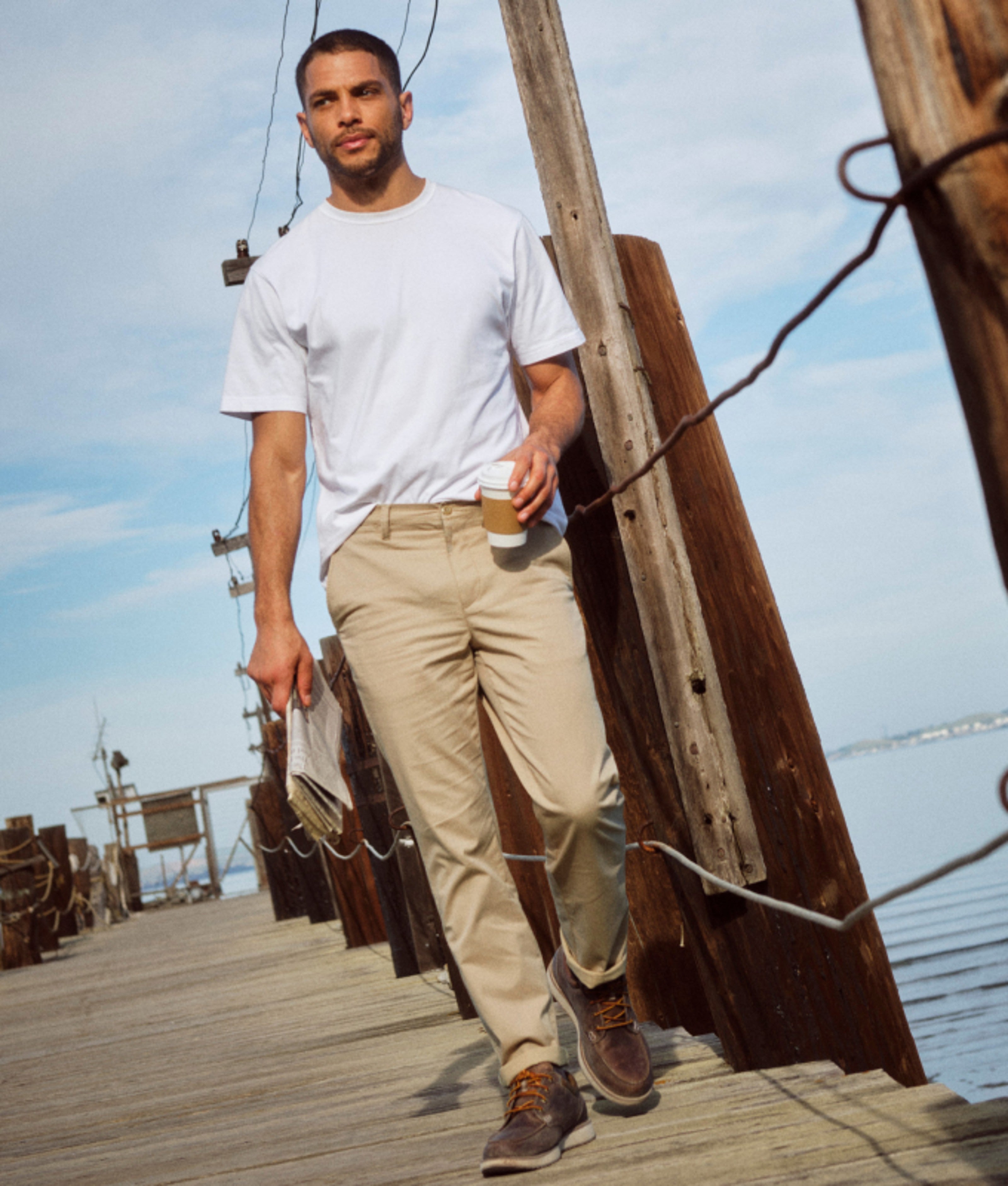 Man walking along a wooden dock in casual pants.