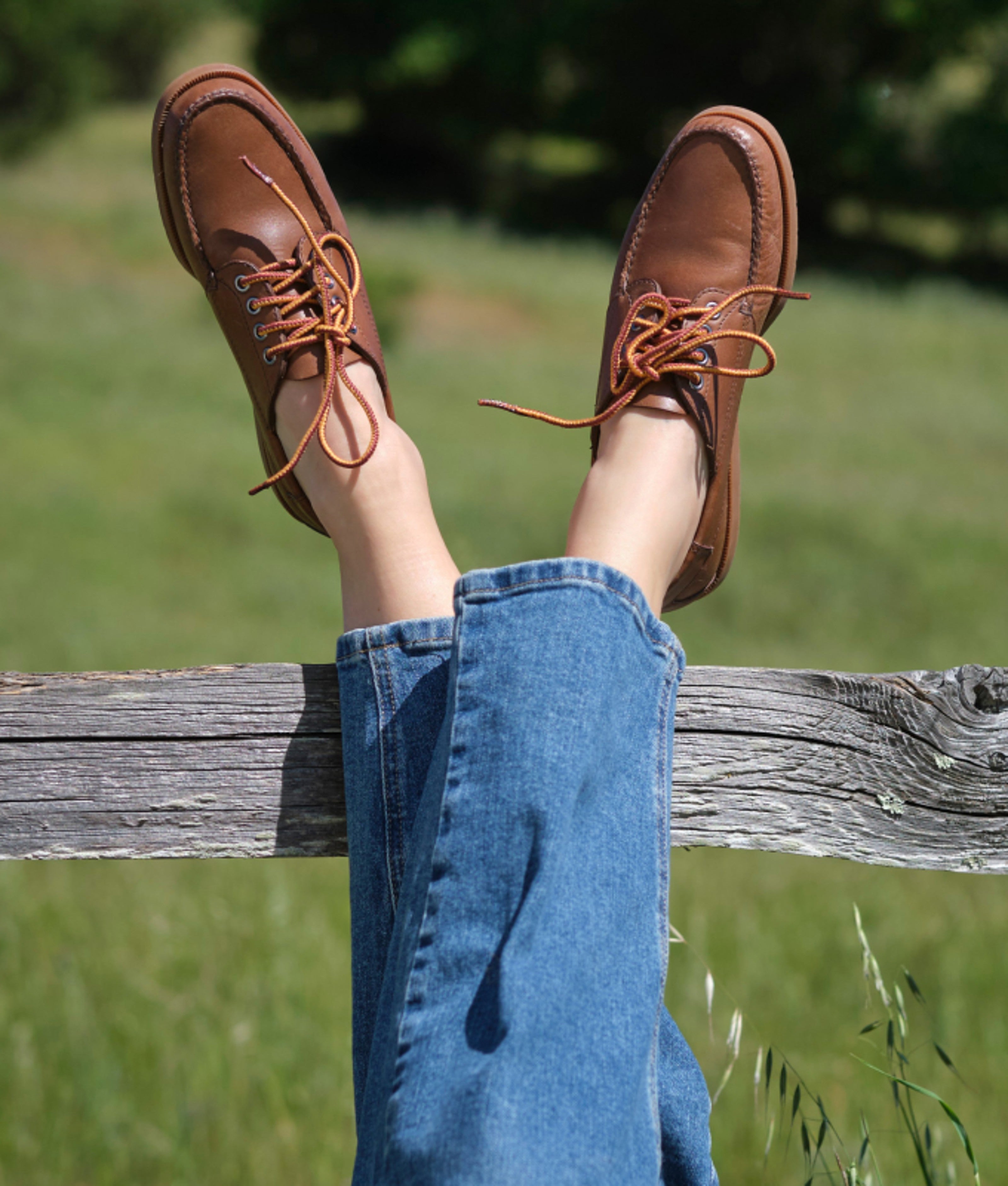 Brown leather footwear resting on a wooden fence rail.