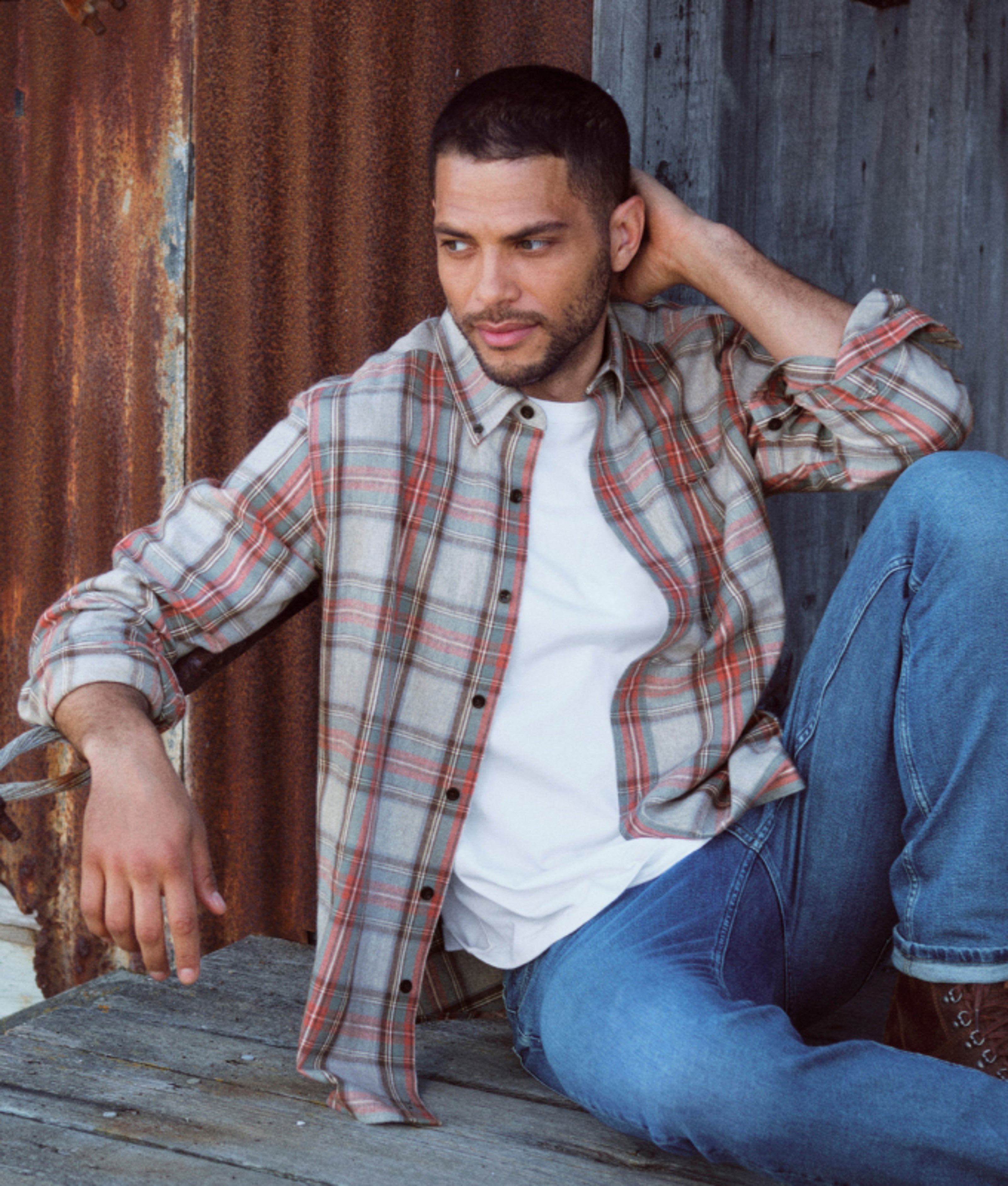 Man seated outdoors wearing a plaid flannel shirt.
